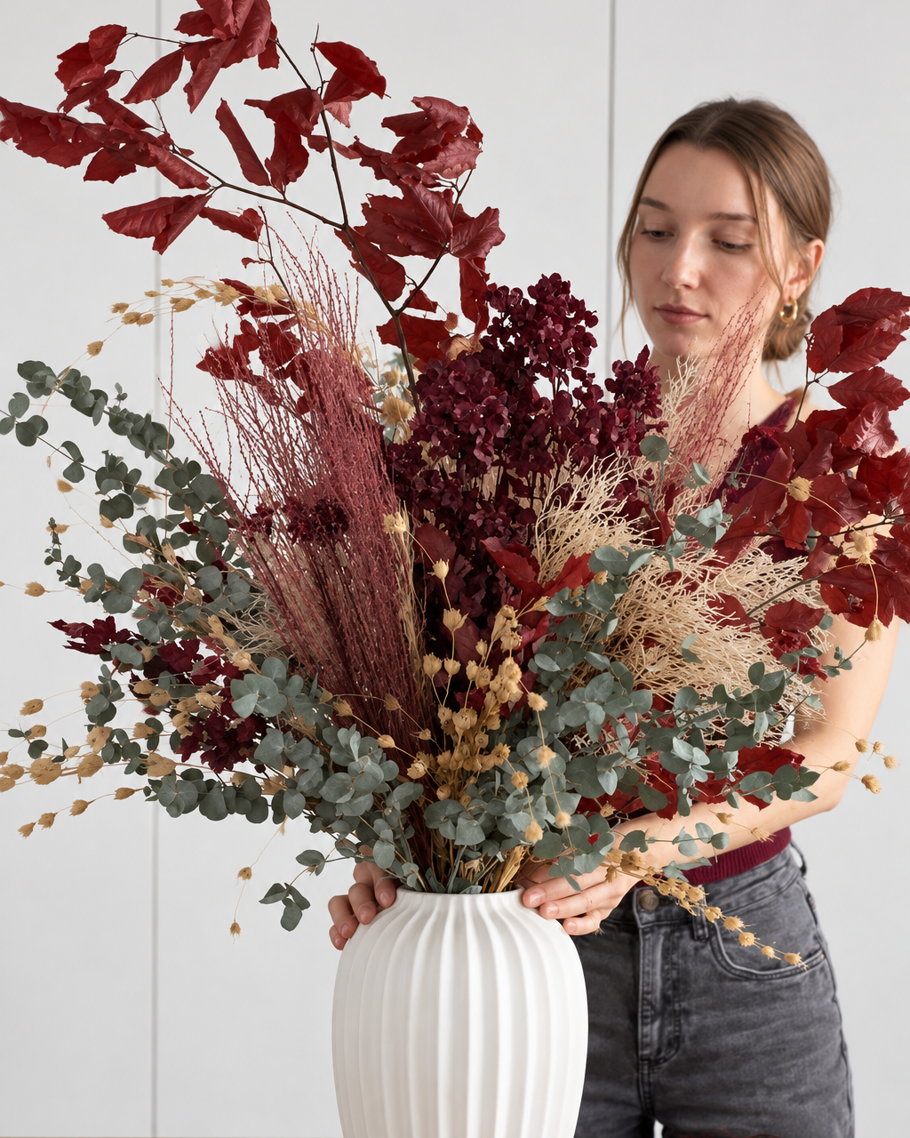 Florist holding the Autumn preserved arrangement of red leaves, grasses and eucalyptus in a white ribbed vase