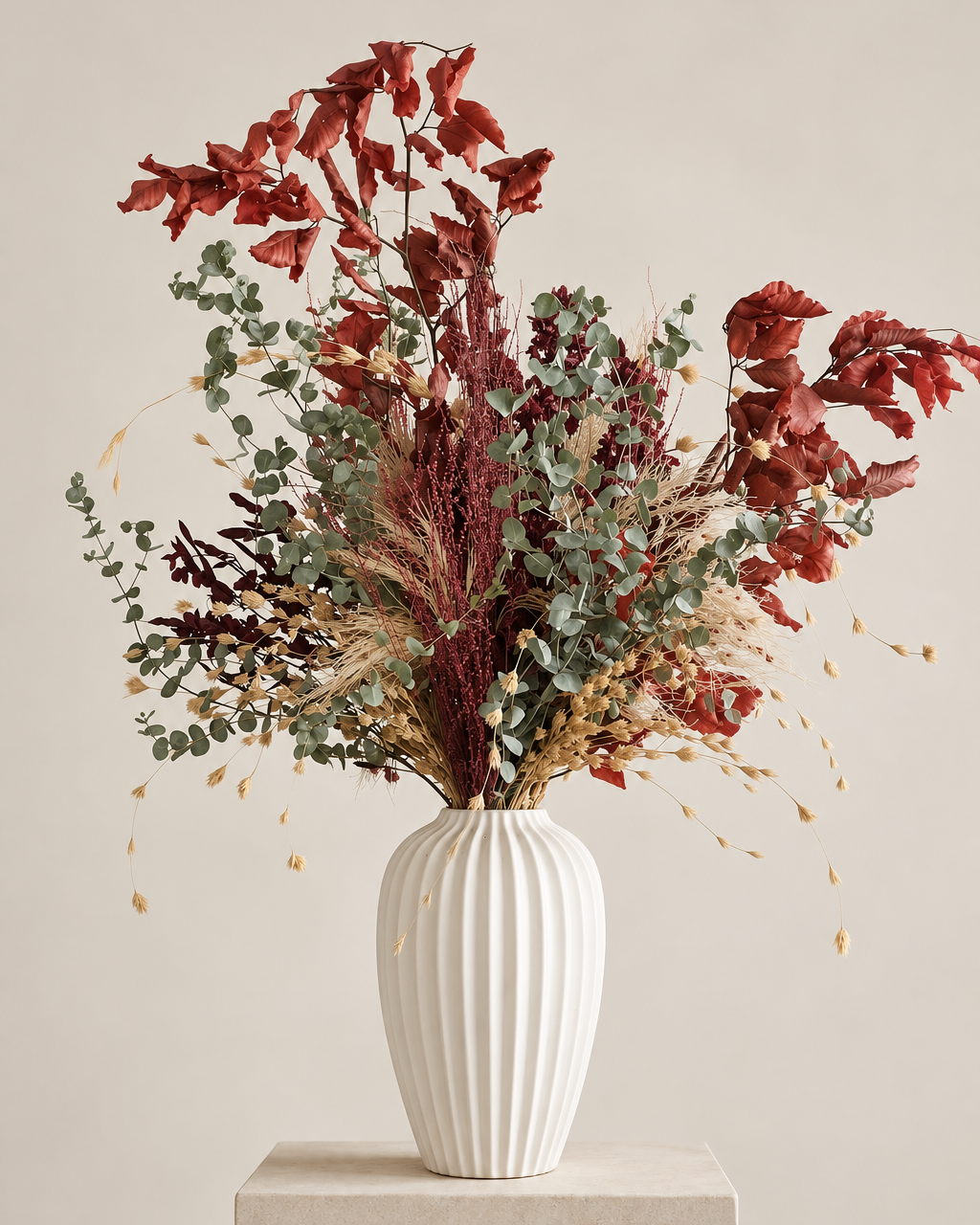 Autumn preserved flower arrangement with rust-red leaves, burgundy blooms and eucalyptus in a ribbed white ceramic vase