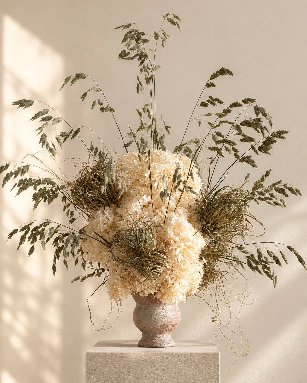 Ecru preserved hydrangea centrepiece with wild oat grasses in a stone-washed ceramic vase on a plinth